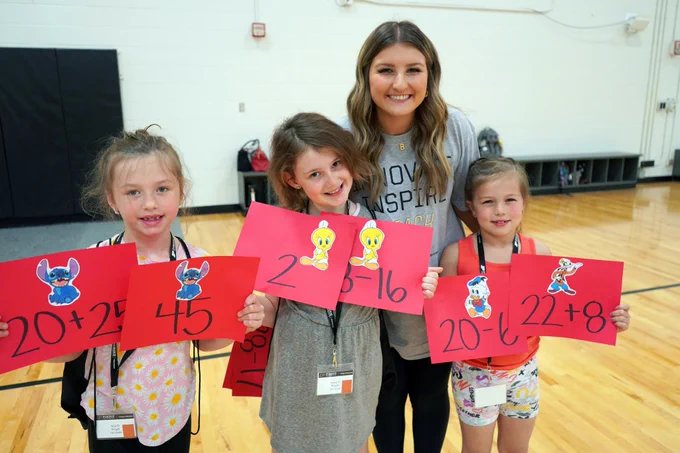 Photo of Purdue Education student with 3 schoolgirls holding up math formulae signs