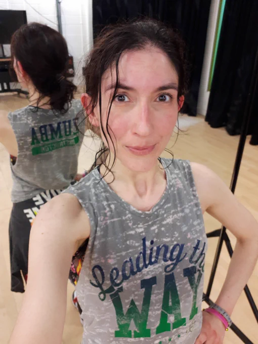 Selfie of Mariana in Zumba clothes looking very sweaty.  Her grey top says 'Leading the way'. There is a mirror behind her.