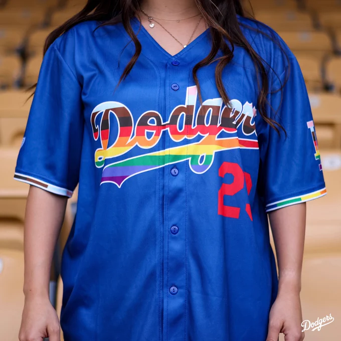 A photo of a blue Dodgers jersey for LGBTQ  Pride Night. The Dodgers logo on the front of the jersey incorporates colors from the pride rainbow flag. It also has the number 23 in red.