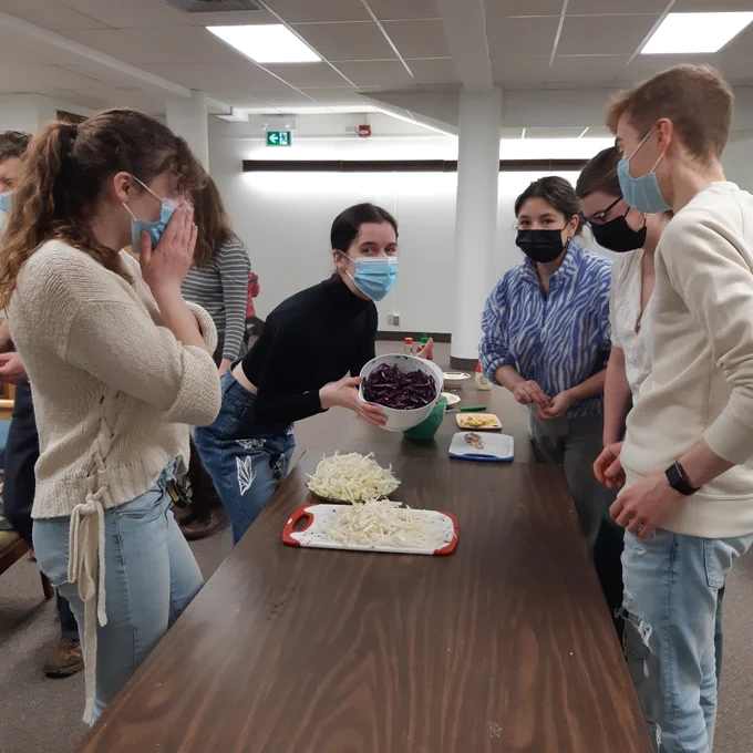 Interior photo of university students standing around a table as they cut up cabbages. 