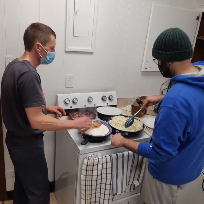 Interior photo of two people standing in a kitchen as they cook cabbage on top of an electric stove.