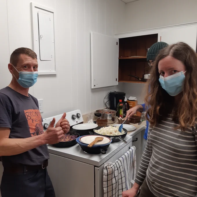 Interior photo of Charles (making two thumbs up sign) and Jessie standing in a kitchen in front of a stove as they cook cabbage.