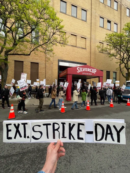 A hand holding a sign reading “EXT. STRIKE - DAY” positioned in front of the May 4, 2023 picket line outside Silvercup Studios in NYC.
