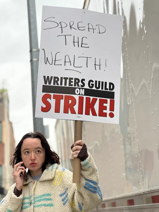 A picketer holding a sign which reads “Spread the WEALTH! Writers Guild on Strike!”
