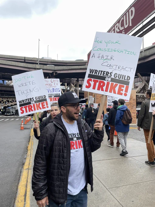 Strikers on the picket line at Silvercup Studios in NYC. The two fully-visible picket signs in the image read “Do the WRITE thing!” and “For your consideration: A fair contract”