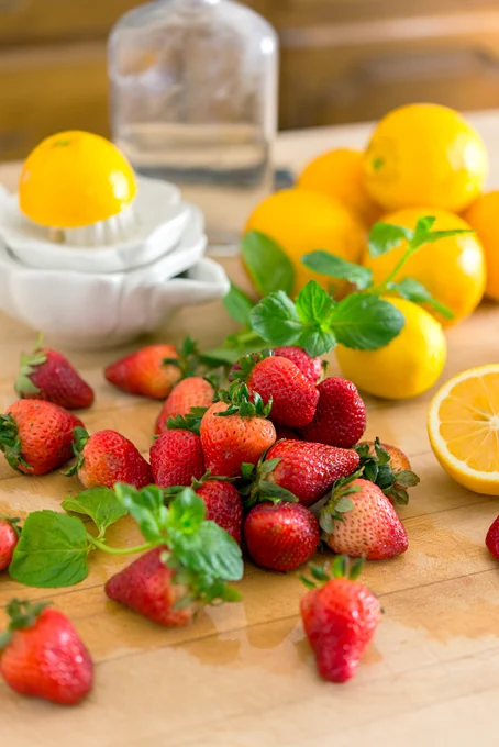 small piles of fresh strawberries, lemons and mint on a chopping block