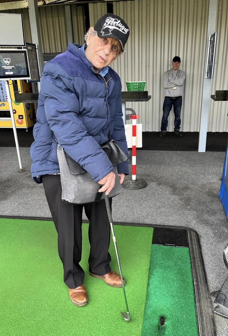 A person is stood on the golf mat. They're holding their golf club and looking at the camera. 