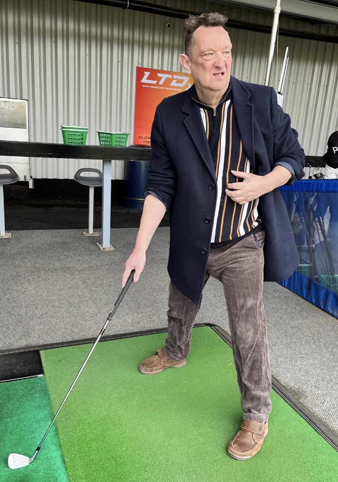 A person is stood on the golf mat, they are looking into the distance to see how far their ball has gone.