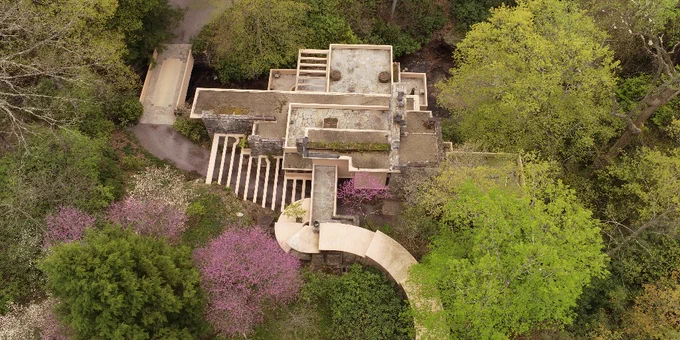 A drone shot of Fallingwater in spring. Redbuds are in full bloom and leaves are vibrant green.