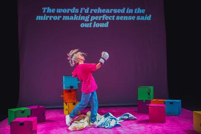 Alice mid motion with white boxing gloves on with coloured jigsaw squares around her. The captions behind her read ‘the words is rehearsed in my head making total sense said out loud’