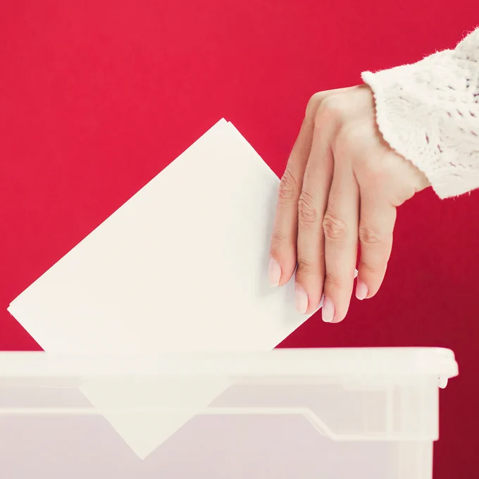 Imagen de la mano de una mujer a punto de introducir su voto en la urna.
