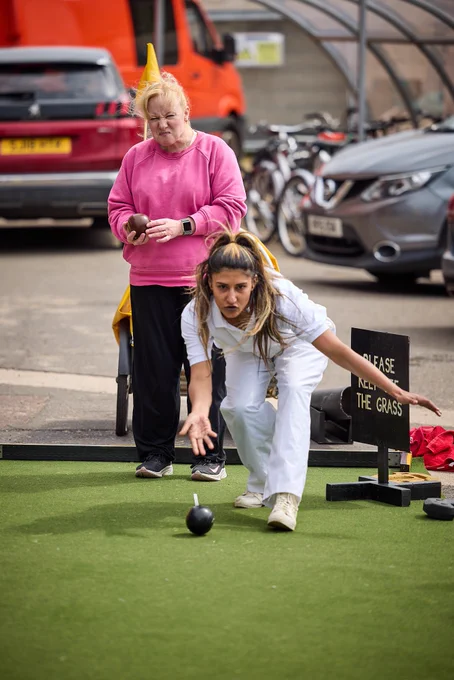 Woman in sports gear launches a bowl towards camera, woman behind looks furious