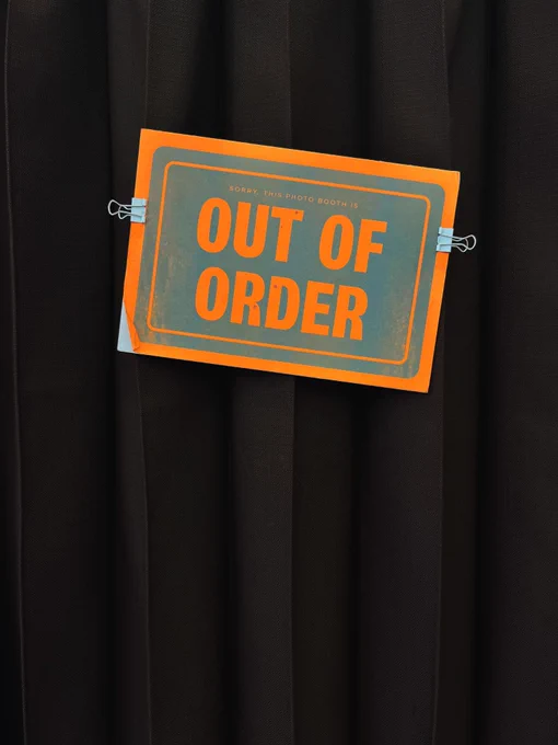An orange and grey sign that says “out of order” hung on the black curtain of a Photo Booth