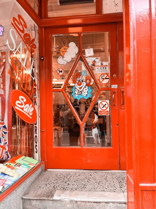 The front door of Clarks Brothers in Manchester. It’s red and has five glass panels. The middle panel is diamond shaped and has a transfer of a clown illustration