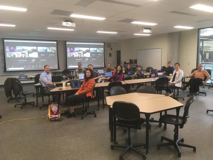 The team in our meeting room (with Zoom attendees shown on screen in front of room)