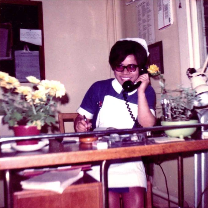 Professor Dame Elizabeth Anionwu in a vintage photo as a nurse. She is wearing uniform and is smiling on the phone.