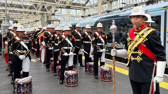 A number of soldiers in dress uniform with instruments stand on a platform at Waterloo.