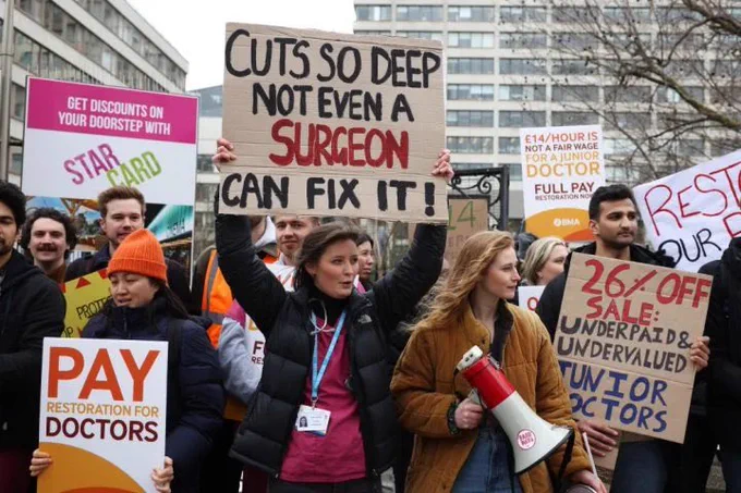 Protesting doctors with signs saying things like “cuts so deep not even a surgeon can fix it!” and “26% off sale: underpaid and undervalued junior doctors” outside St Thomas’s hospital