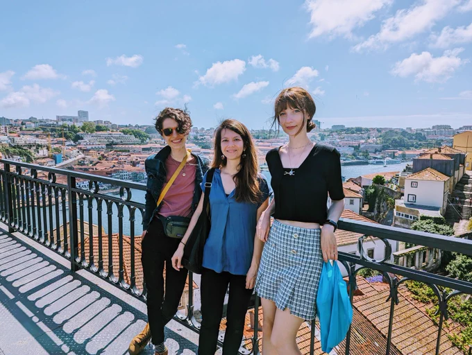Three women smiling, on a bridge with Porto City view in the background and lovely blue sky. 