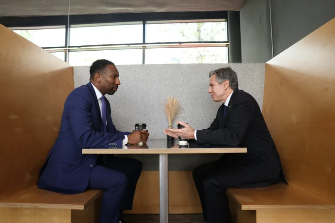 Secretary Blinken and Atlanta Mayor Andre Dickens drink coffee and share a conversation while sitting in a sleek wooden booth at Refuge Coffee.