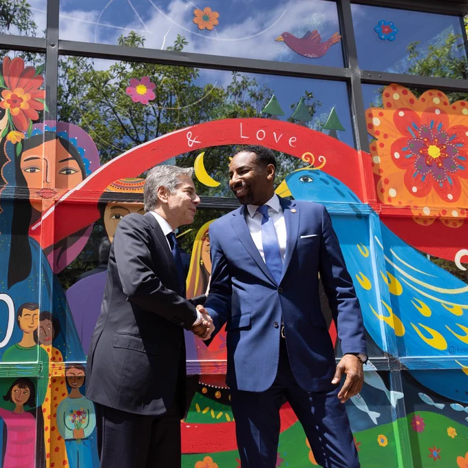 Secretary Blinken and Atlanta Mayor Andre Dickens smile and shake hands while standing in front a colorful Refuge Coffee mural.