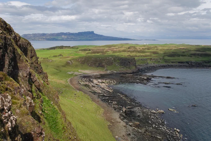 looking down on a rocky beach with skerries, green slopes and distant island