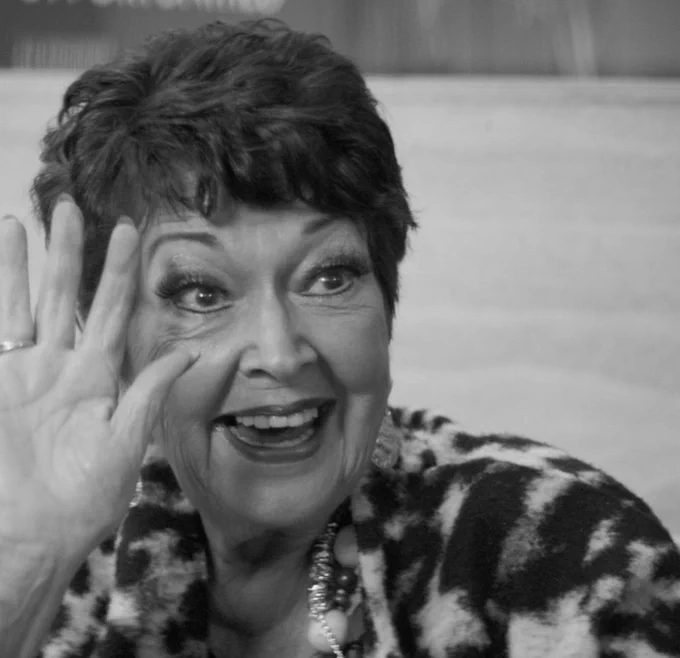 Ruth Madoc smiles and waves in black and white