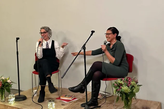 Photo of me on a stage with my friend Pamela. We're seated with microphones and pointing at each other.
