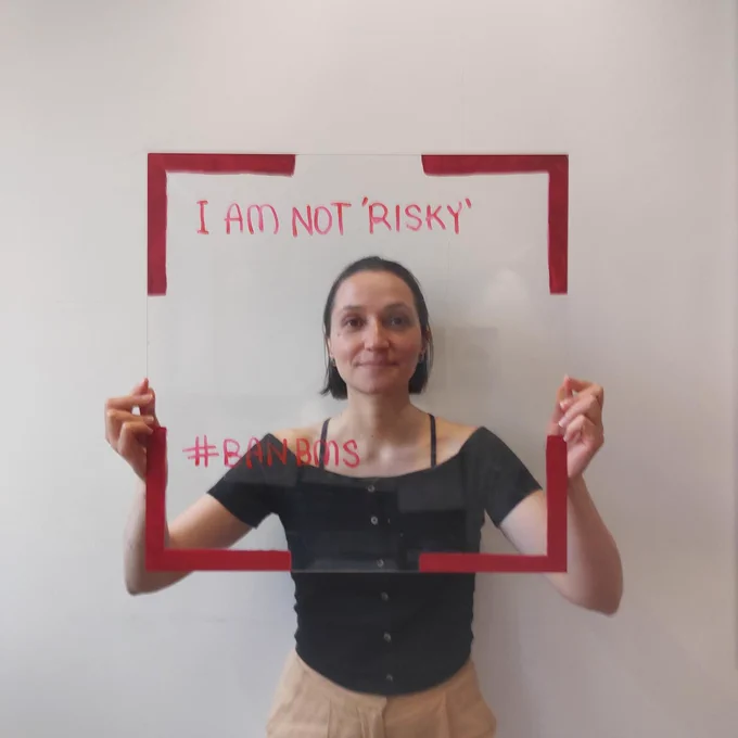 A woman holds a frame with red egdes and the words 'I am not 'risky' and #BanBMS'