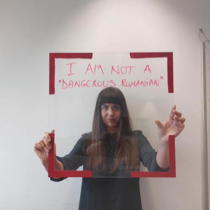 A woman holds a frame with red egdes and the words 'I am not a 'dangerous romanian''