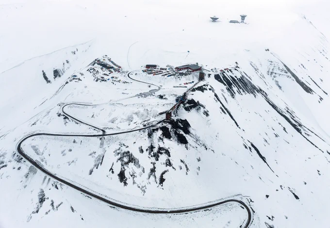 Ilmakuva lumipeitteisestä vuoresta, jolla mutkittelee tie. Kuva: Marcel Schütz / Svalbard Photography.
