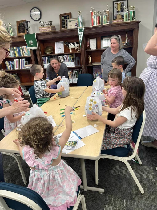 children at a table holding gallon cartons filled filled with dirt.