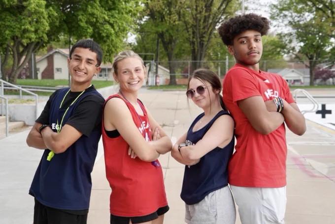 Four lifeguards stand back to back with their arms crossed. 