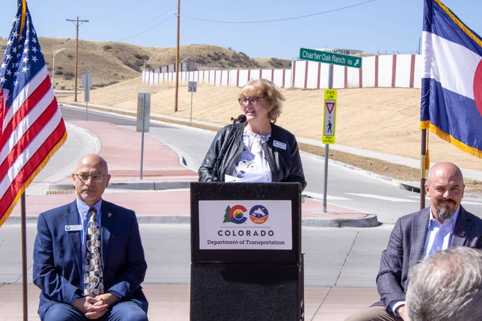 Fountain Mayor and Pikes Peak Area Council of Governments Chair Sharon Thompson speaking at a podium with the American and Colorado flags behind her.