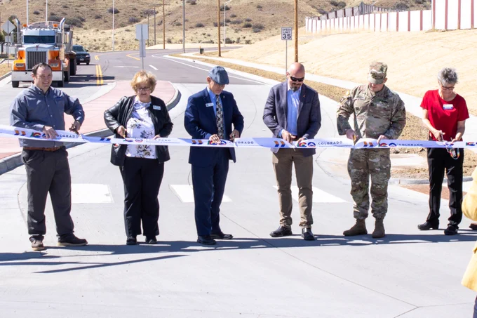 A group of six people cut a large ribbon on a roadway.