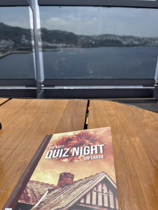 A copy of the play text “The Last Quiz Night on Earth” by Alison Carr on a table overlooking the sea and a Greek Island