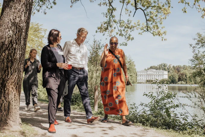 A photo of Cohort 6 Chair Sir David Behan in conversation with Sciana Fellows while on a walk around the lake adjacent to Schloss Leopoldskron. 