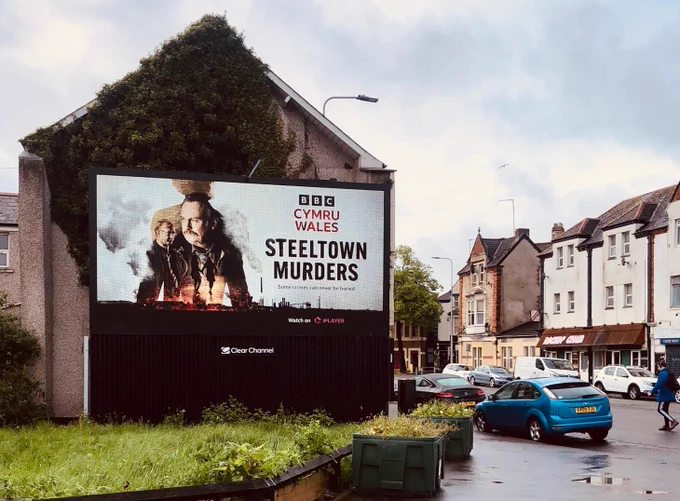 Picture of advertising hoarding for BBC drama Steeltown Murders seen on side of house. 