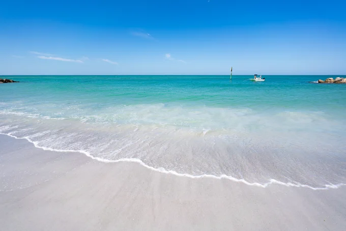 A gentle wave washes ashore of Upham Beach on a bright sunny day,