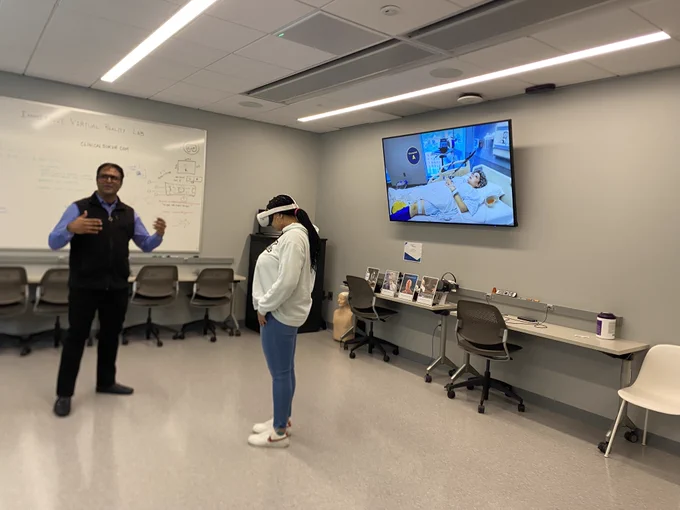 Woman wearing a white hoodie is wearing VR goggles in a simulation lab