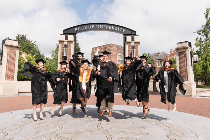 A group of graduates celebrating in front of the arch on a sunny day.