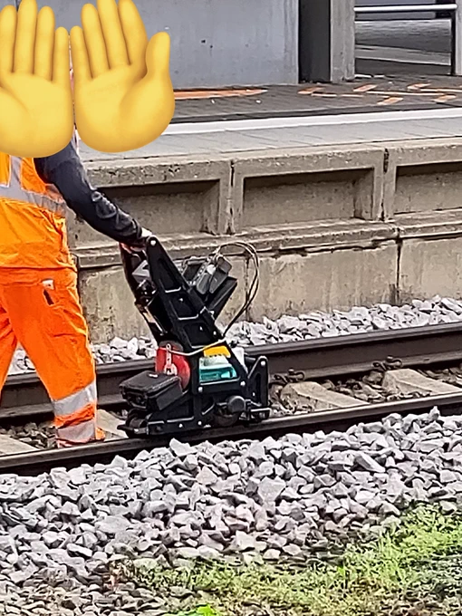 Eine Person schiebt eine Art Wagen über die Schienen am Bahnhof 