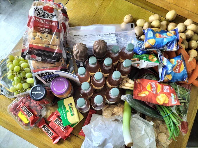 A massive pile of food. Including: carrots potatoes parsnips cucumber leek lettuce grapes walkers crisps chocolate bars spray cream kombucha bread loads of packets of biscuits butter tissues spring onions raspberries croissants curry sauce passatta 