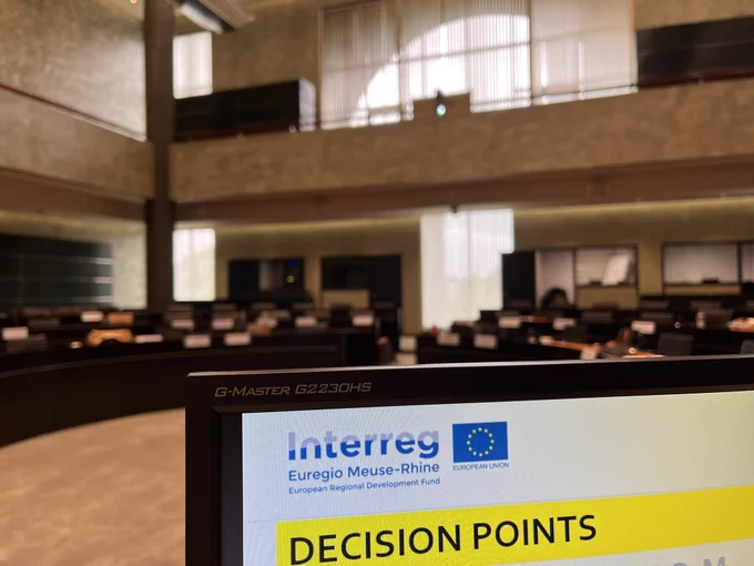 Blick in den noch leeren Saal. Im Vordergrund ein Bildschirm mit dem Logo des Programms und der englischen Überschrift Decision points.