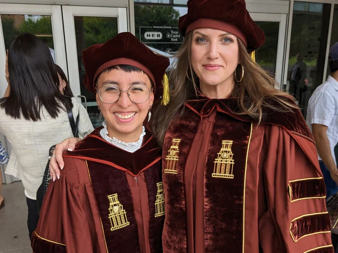 Performance as Public Practice graduates siri gurudev and Molly Roy pose together wearing their Ph.D. regalia