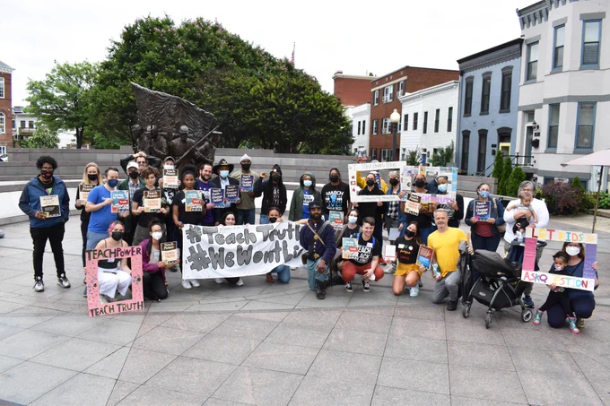 Group of people kneeling in front of the African America Civil War Memorial in D.C. They are holding signs that read "#TeachTruth" and similar messages defending social justice education