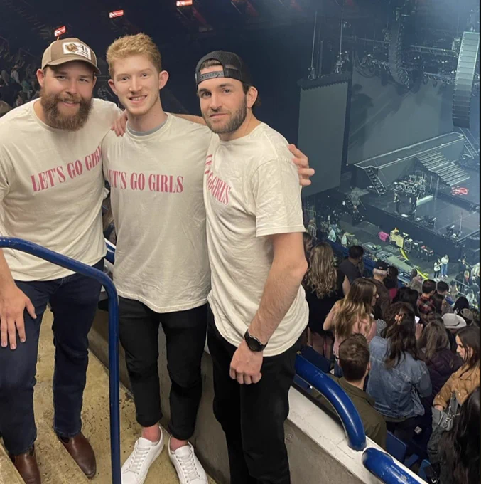 Mitch McLain, Dustin Wolf, and Alex Gallant posing with Let’s Go Girls shirts, standing on the balcony in the Saddledome with the Shania Twain stage behind them