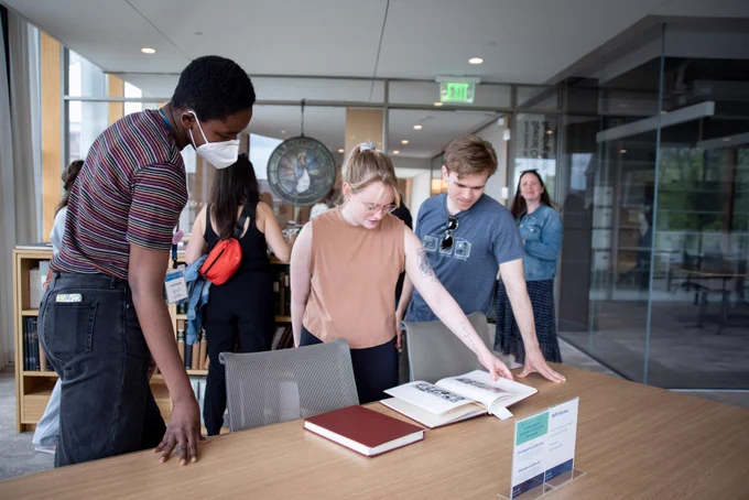 Three people observe a Smith College yearbook on display in the Special Collections Reading Room