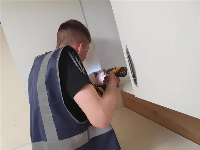 Student wearing a high vis drilling into a cupboard 