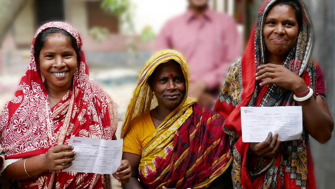 Three women hold up banking slips.